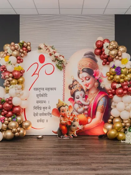 This is a beautiful example of a traditional Godh Bharai or baby shower decoration. The backdrop features a serene illustration of a mother and Ganesha, framed by an elegant balloon arrangement in white, gold, and maroon.