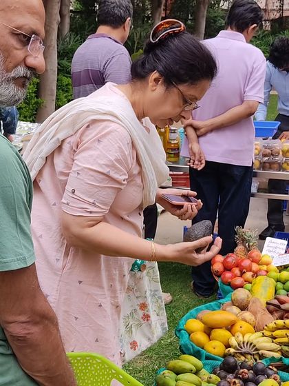 A customer inspecting an avocado at a stall laden with tropical fruits like pineapple and mangosteen.