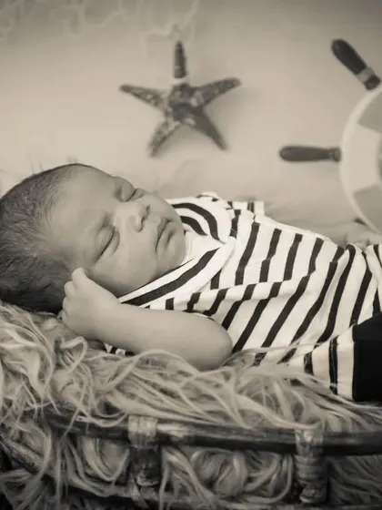 A classic black and white portrait of a newborn baby in a sailor outfit, sleeping in a basket with nautical props.