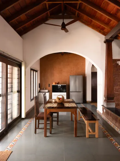 A view of the dining hall in our Vinaya residence project. This space is defined by an arch leading to the kitchen, a high vaulted wooden ceiling, and a Lohi lime plaster accent wall, demonstrating how natural materials create warm and functional living areas.