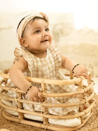 A happy baby girl in a wicker basket, part of our rustic and natural-themed milestone sessions.