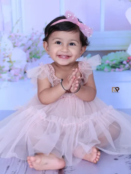A close-up of a happy baby girl in a pink fairy dress, clapping her hands with joy. The soft, dreamy background enhances the magical feel of the portrait.