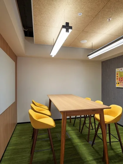 This collaboration space features a high table with yellow stools and a large whiteboard for brainstorming. The wood-fiber acoustic panels on the ceiling help to manage sound.