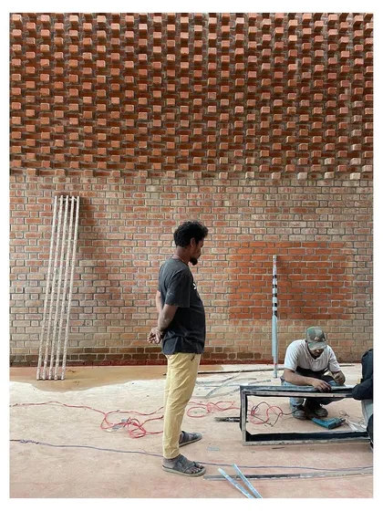 Workers installing lighting fixtures against a textured brick wall, showcasing the process of layering technical systems into the architecture.