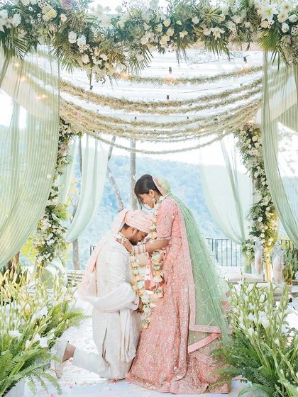 A groom bows down to touch the bride's feet during the varmala ceremony, a modern and respectful gesture of love.