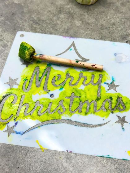 The tools of festive creation: a "Merry Christmas" stencil covered in paint after a fun card-making session.