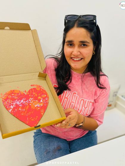 A happy participant shows off her vibrant red and orange heart canvas. Fluid art is a great way to let go and create without a rigid plan.