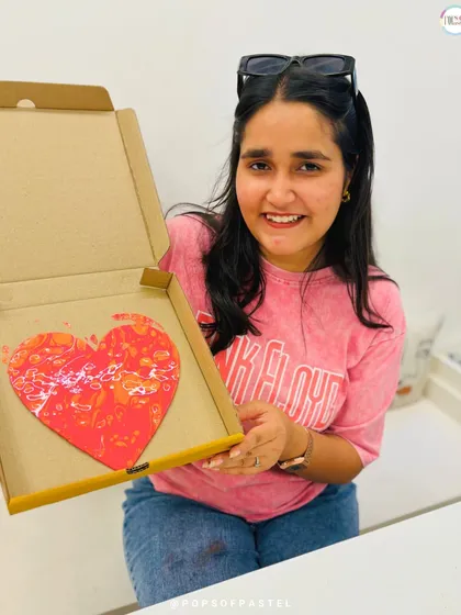 A happy participant shows off her vibrant red and orange heart canvas. Fluid art is a great way to let go and create without a rigid plan.