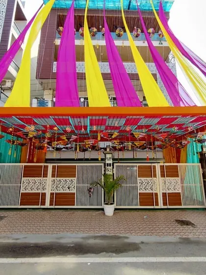 For traditional ceremonies, we create grand entrances. This setup features a full pipe pandaal structure with vibrant yellow, pink, and orange fabric draping and decorative hangings to welcome guests.