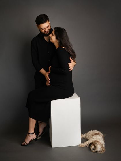 A complete family portrait, including their adorable fur baby sleeping at their feet. This shot captures the love and connection of the entire growing family in a modern studio setting.