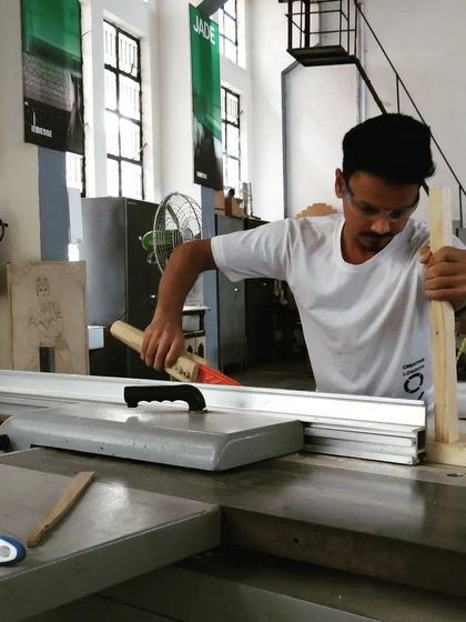 Wearing safety glasses, a student uses a push stick to safely guide a piece of wood through the table saw, demonstrating proper safety protocol.