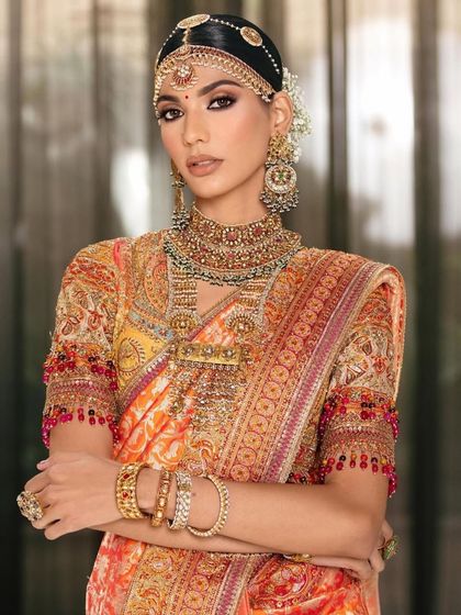 A full-length view of a stunning South Indian bridal look. The makeup is designed to complement the rich colours of the saree and the heavy temple jewellery.