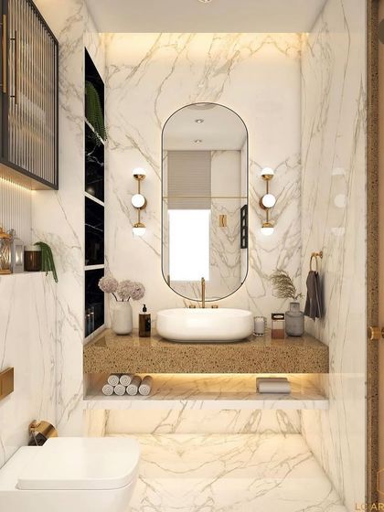 A bright and elegant bathroom with white marble walls and gold accents. The design features a floating vanity, an oval mirror with sconces, and a fluted glass storage cabinet.