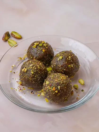 Healthy date and pistachio energy balls, lightly garnished with crushed pistachios on a clear glass plate. This clean shot is perfect for showcasing healthy dessert alternatives or snacks.