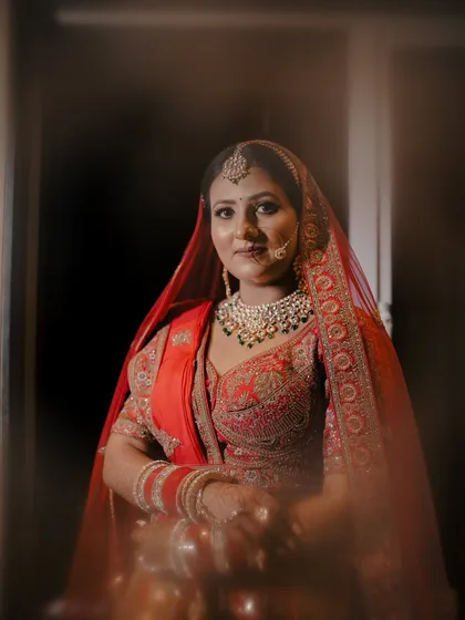 A soft and classic bridal portrait. The focus is on the bride's calm expression and the beautiful details of her red lehenga and jewelry.