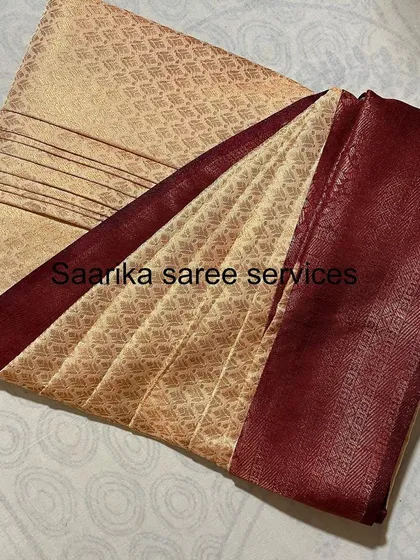 A beige saree with a deep maroon border, folded by Saarika Saree Services.
