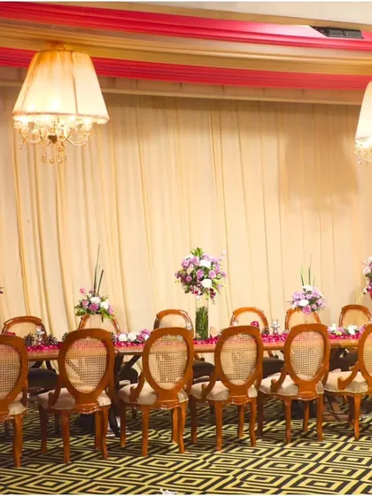 A long, beautifully decorated dining table ready for guests. This setup, with its floral centerpieces and classic chairs, is perfect for a formal, seated dinner.