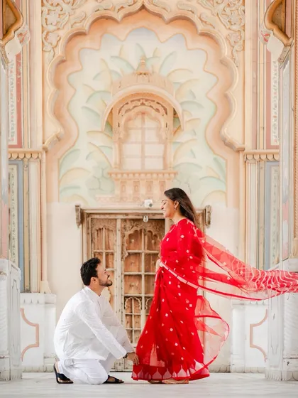 Against the magnificent arches of Jaipur's Patrika Gate, he asked for her forever. The vibrant red of her saree and the grandeur of the setting create a truly royal proposal photograph.