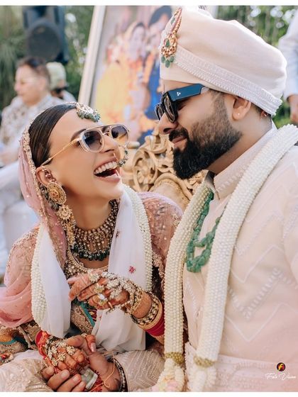 A candid and happy moment of the couple during their wedding ceremony, both wearing sunglasses and sharing a laugh.
