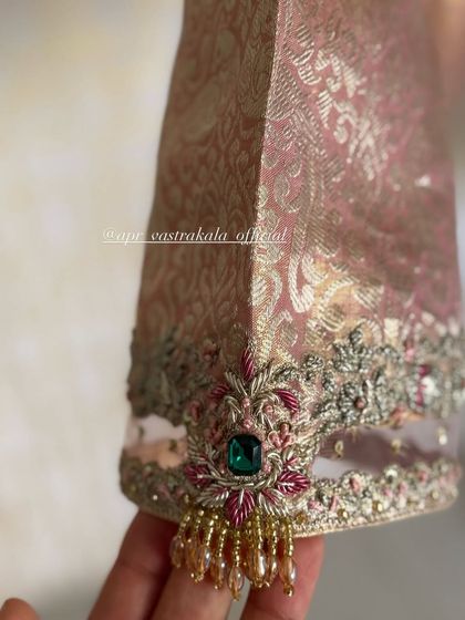 A close-up of a sleeve cuff featuring delicate zardosi, emerald green stones, and pearl tassels. This shows the fine details that go into each piece.