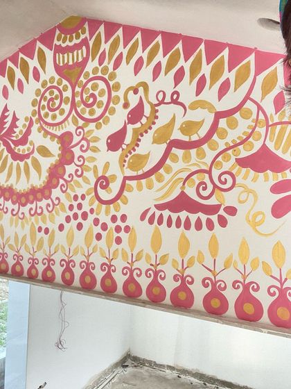 A selfie with a section of the 'Baba's Garden' mural. The combination of gold and pink on the white wall creates a festive and welcoming feel, perfect for this outdoor space.