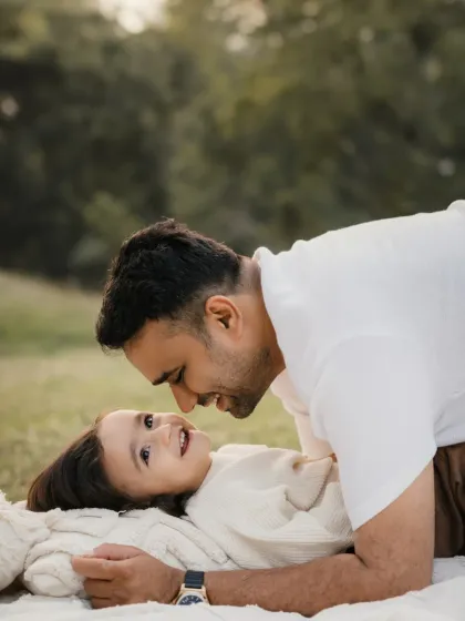 A father and child share a loving gaze while lying on a blanket. This intimate portrait captures a quiet moment of connection.