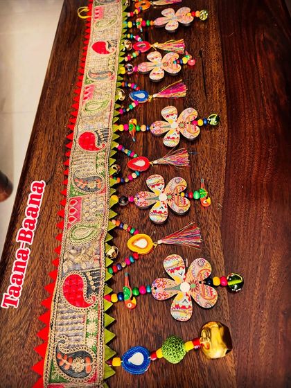 A detailed view of the 'Taana Baana' toran, showing its playful, asymmetrical design. The dancing flowers, mirror garlands, and colorful beads come together to create a piece that is pure, chaotic beauty.