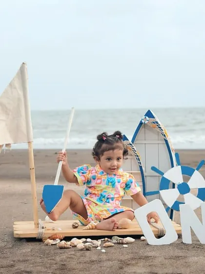 A little girl playing with a shovel and shells during her nautical-themed first birthday shoot on the beach.