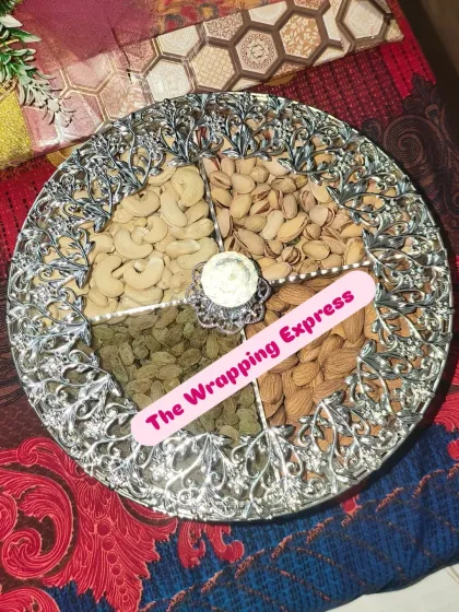 A classic dry fruit platter presented in an elegant silver-finish dish, with separate sections for cashews, pistachios, almonds, and raisins.
