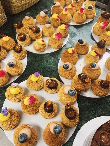 An assortment of our choux pastries, beautifully plated and garnished with fresh berries, edible flowers, and rose petals. They are perfect for dessert tables and gifting.