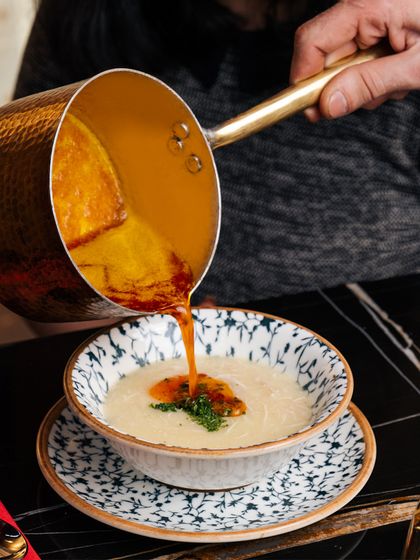 The final touch of flavor. A rich, spiced oil is poured over a creamy soup, showcasing our attention to detail and commitment to building layers of flavor in every dish.