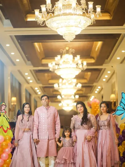 A grand family portrait at Purvi's 5th birthday celebration. The whole family wore matching pink outfits, standing under beautiful chandeliers.