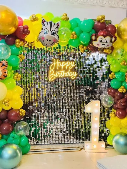 A jungle animal theme with a glamorous twist. This setup features a gold shimmer wall, a neon sign, and a colorful balloon garland with animal head foil balloons.