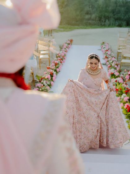 A beautiful shot of the bride walking towards the groom, captured from his perspective. Her joyful expression as she lifts her lehenga is a perfect, candid moment.