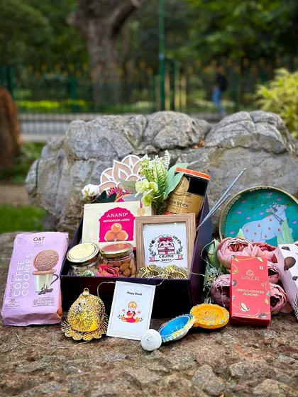 This vibrant Diwali gift box is curated to delight the senses. It brings together a mix of traditional and modern treats, including coffee cookies, assorted nuts, sweets, and festive decor like a hand-painted diya and a framed logo. It’s a complete festive celebration in a box.