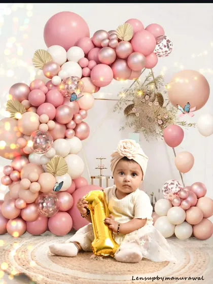 Celebrating a magical first birthday with a beautiful balloon arch setup in shades of pink and white, this portrait captures the sweet innocence of a one-year-old's major milestone.