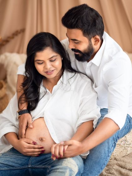 A close-up, intimate moment between a couple in casual jeans and white shirts, focusing on their hands caressing the baby bump.
