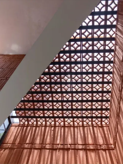 A beautiful terracotta jali screen at the Gifty Residence, viewed from below. This traditional element is used to create privacy, allow for cross-ventilation, and cast intricate patterns of light and shadow.