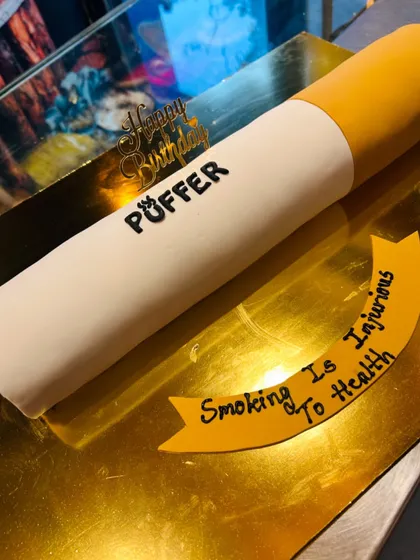 A novelty cake designed to look like a giant cigarette, with a humorous "Smoking is Injurious to Health" message.
