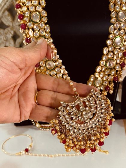 A close-up of a beautiful chand-style maang tikka with ruby bead drops, part of a larger bridal set.