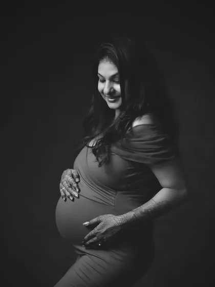 A modern, minimalist black and white portrait. Stripping away color allows us to focus on the form, the emotion, and the beautiful silhouette of the baby bump. The intricate henna on her hands adds a touch of tradition to this contemporary style.