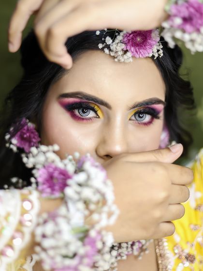 A vibrant Haldi or Mehendi look, featuring bright yellow and purple eyeshadow and floral jewelry.