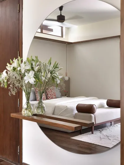 A large, circular mirror with an integrated shelf reflects the serene primary bedroom in 'A Walk in the Clouds', showcasing the custom bed and minimalist design.
