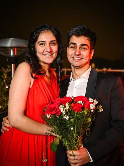The happy couple after she said yes, holding a bouquet of red roses and smiling for the camera.