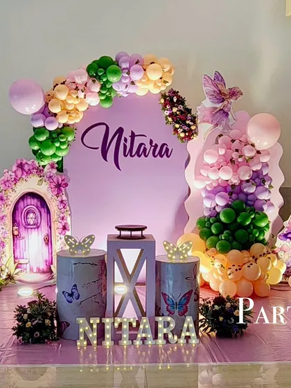 An enchanting fairy-themed birthday party in shades of purple and green. The decor includes a magical door prop, butterfly accents, and a custom name sign.