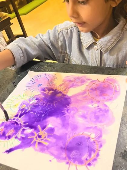 A student carefully paints over her sun drawings, creating a beautiful purple sky. This is a great way to learn about wax-resist techniques.