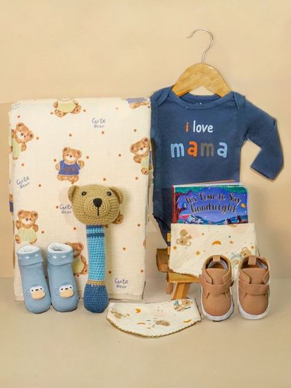 A baby boy hamper featuring an 'I love Mama' onesie and other bear-themed items. The styling is simple and sweet, focusing on the cute products.