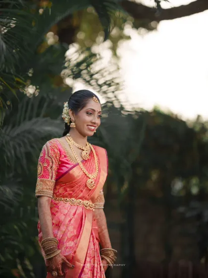 A radiant South Indian bride in her pink silk saree, glowing in the beautiful outdoor light.