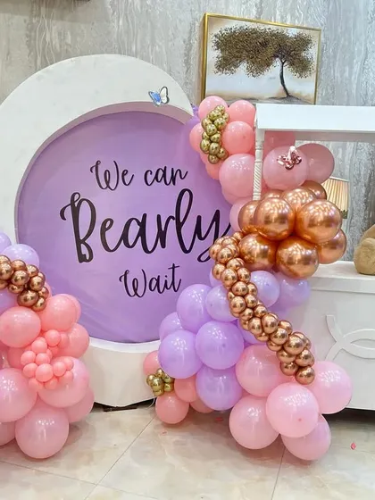This charming setup combines a custom circular backdrop with a cute cart and teddy bear prop. The balloon garland in shades of pink, lavender, and rose gold adds a touch of modern elegance.
