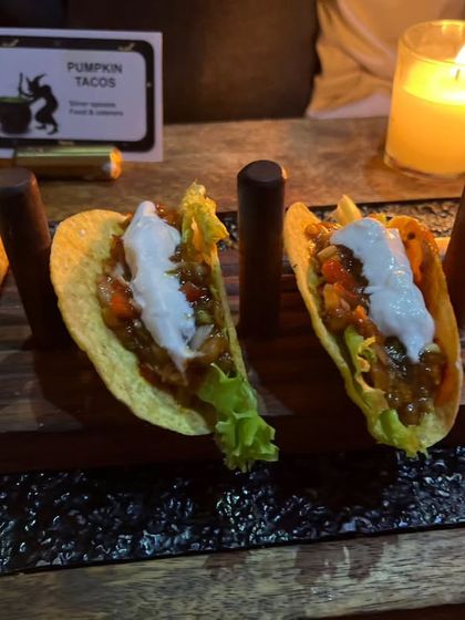'Pumpkin Tacos' served on a rustic wooden stand. This dish perfectly captures the essence of Halloween, combining a seasonal flavor with a crowd-pleasing format.